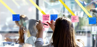 Dame som setter Post-it® Super Sticky Note, 76 mm x 76 mm på glassvegg for å dele oppgaver med andre medlemmer av teamet eller prosjekter